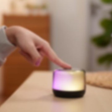 A finger touching a glowing smart speaker