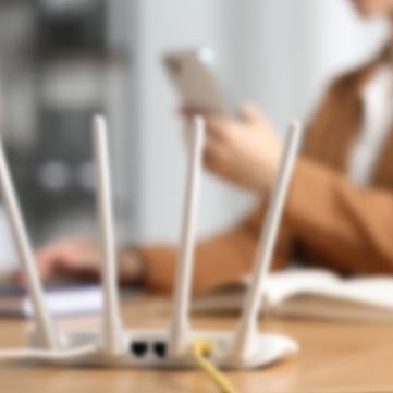A Wi-Fi router on a desk with someone using a phone behind it